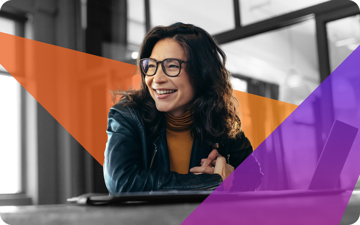 A woman with long hair and glasses smiles while leaning on a table. Shes wearing a leather jacket and an orange turtleneck. The image features abstract orange and purple geometric shapes overlayed on it.