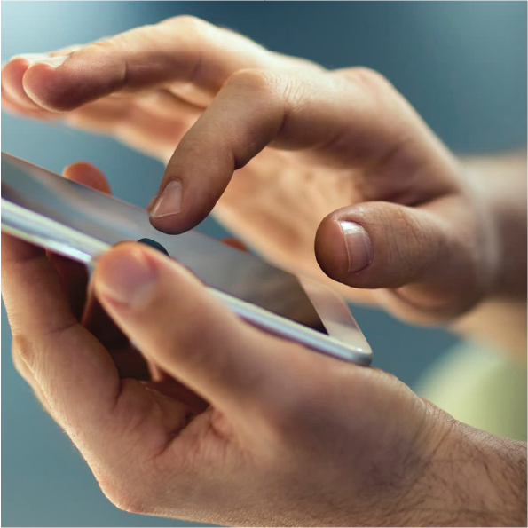 Close-up of a person holding a smartphone with both hands, using their thumb to interact with the screen. The background is softly blurred with shades of blue and green.