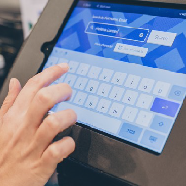 Close-up of a persons hand typing on a touchscreen keyboard, searching for Helena Lauren on a digital interface. The background is slightly blurred, focusing on the screen and hand.