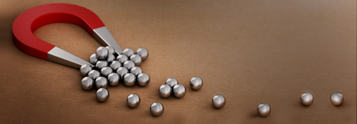 A red horseshoe magnet, symbolizing employee retention, attracts several small silver metallic spheres on a brown surface. Some spheres are clumped near the magnet, representing loyal team members, while a few others are spaced out in a line.