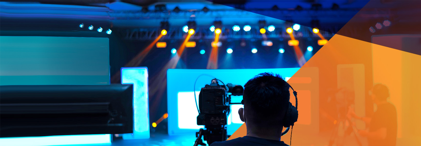 A person operates a professional camera in a dimly lit event space, reminiscent of scenarios in the Virtual Meetings Playbook. The background features colorful stage lights in blue and orange hues, illuminating the scene and highlighting several large, blurry screens.
