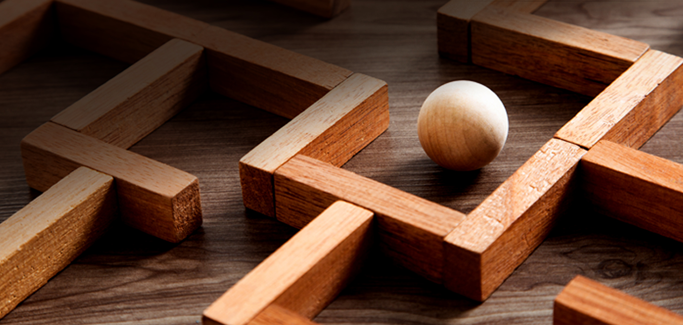A wooden maze with a smooth, round ball positioned near a corner, reminiscent of navigating the challenging paths in sales training. The maze consists of intricately arranged rectangular blocks on a wooden surface.