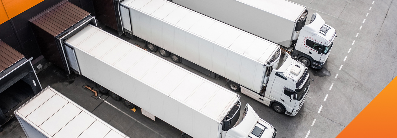 Aerial view of four white semi-trailer trucks parked in a row at a loading dock, showcasing efficient logistics operations that could benefit from channel incentive programs to boost productivity and collaboration.